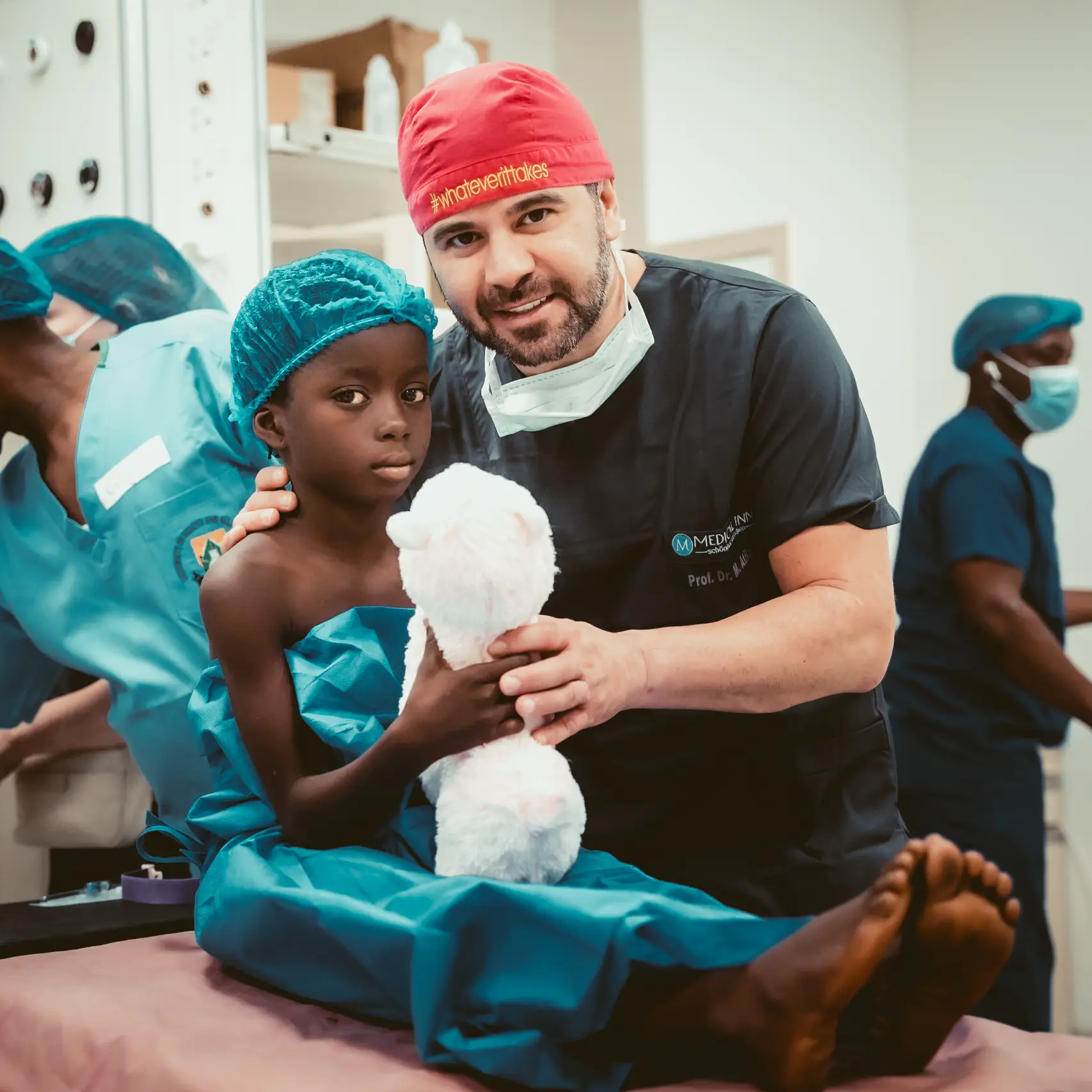 Prof. Dr. Mehmet Atila mit einem Kind und Teddybär im Operationssaal