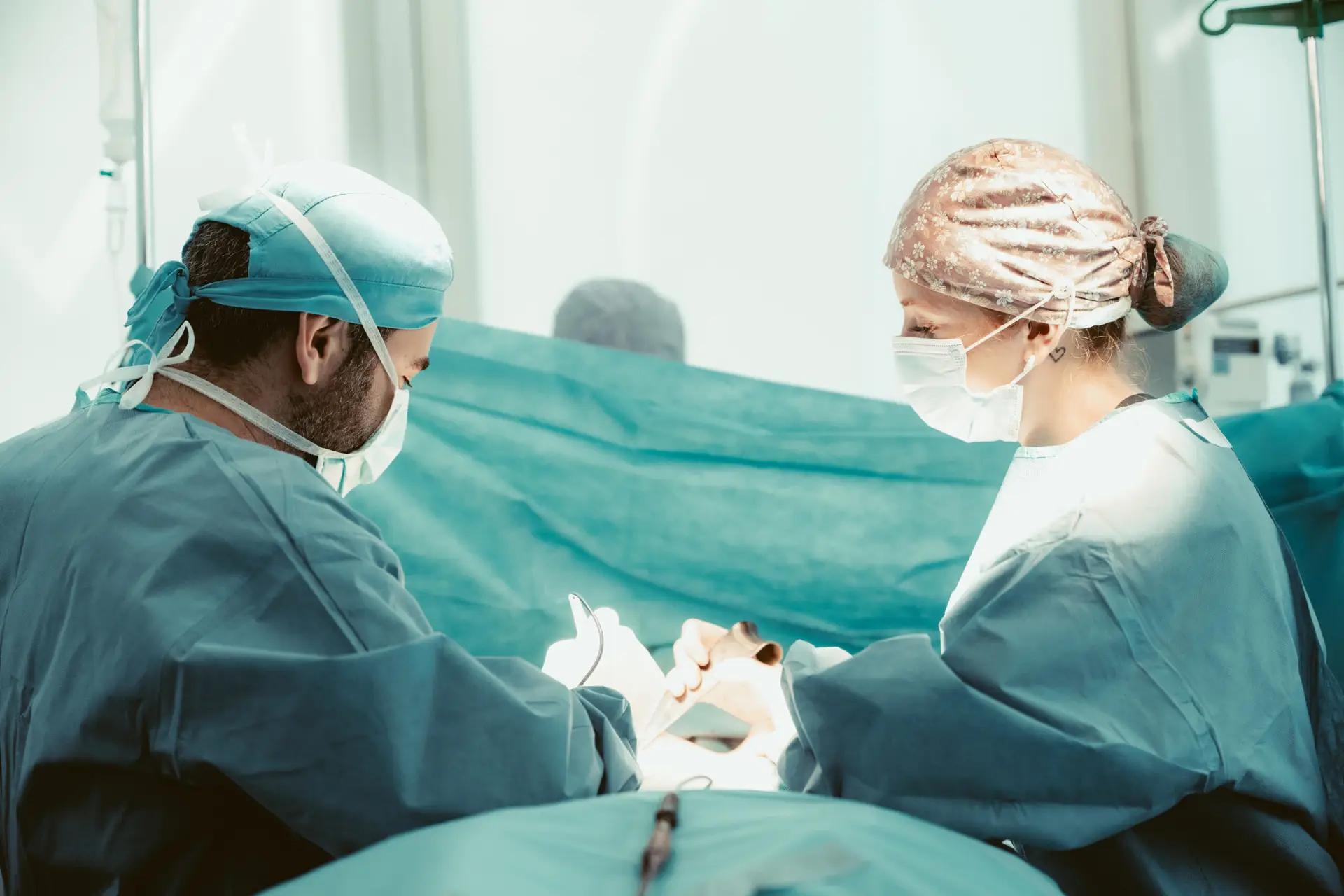 Zwei Operateure mit OP-Hauben und Mundschutz während eines chirurgischen Eingriffs