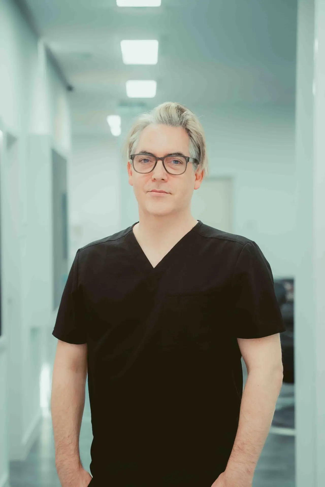 Dr. Daniel Thieme mit Brille in schwarzer Arztkleidung in den Praxisräumen