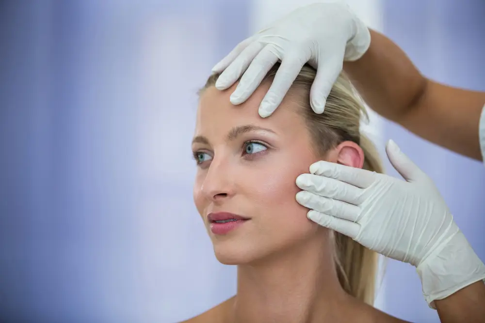 Ärztliche Untersuchung des Gesichts einer Frau mit behandschuhten Händen vor einem Facelift